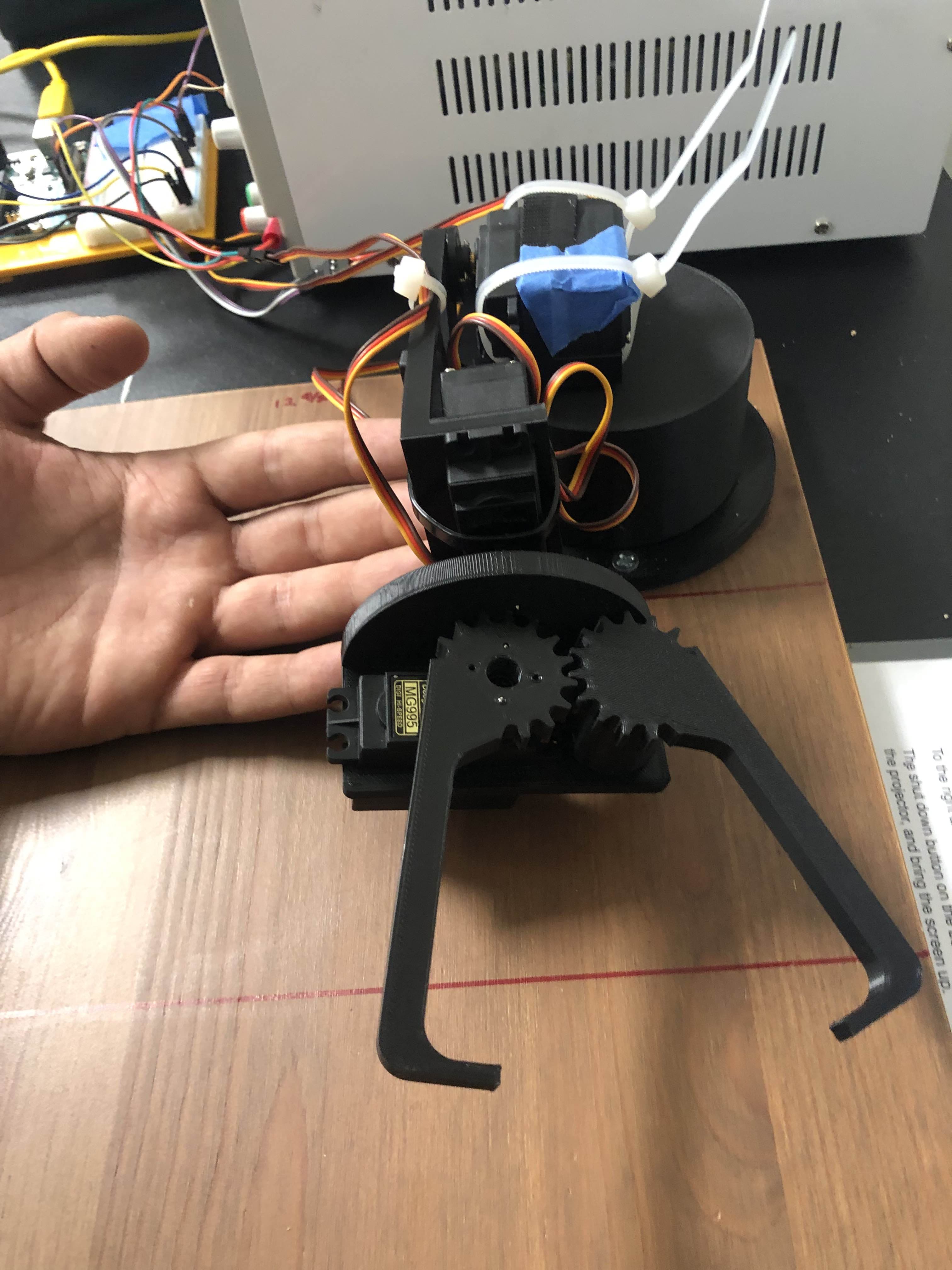 Can Arm gripper next to a hand for scale on the workbench